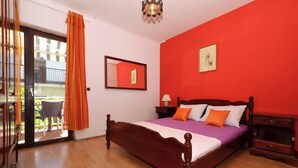 Quarto com cama de madeira, parede vermelha e varanda com cortinas laranja.