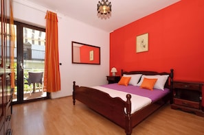 Une chambre avec un lit en bois, un mur rouge et un balcon agrémenté de rideaux orange.