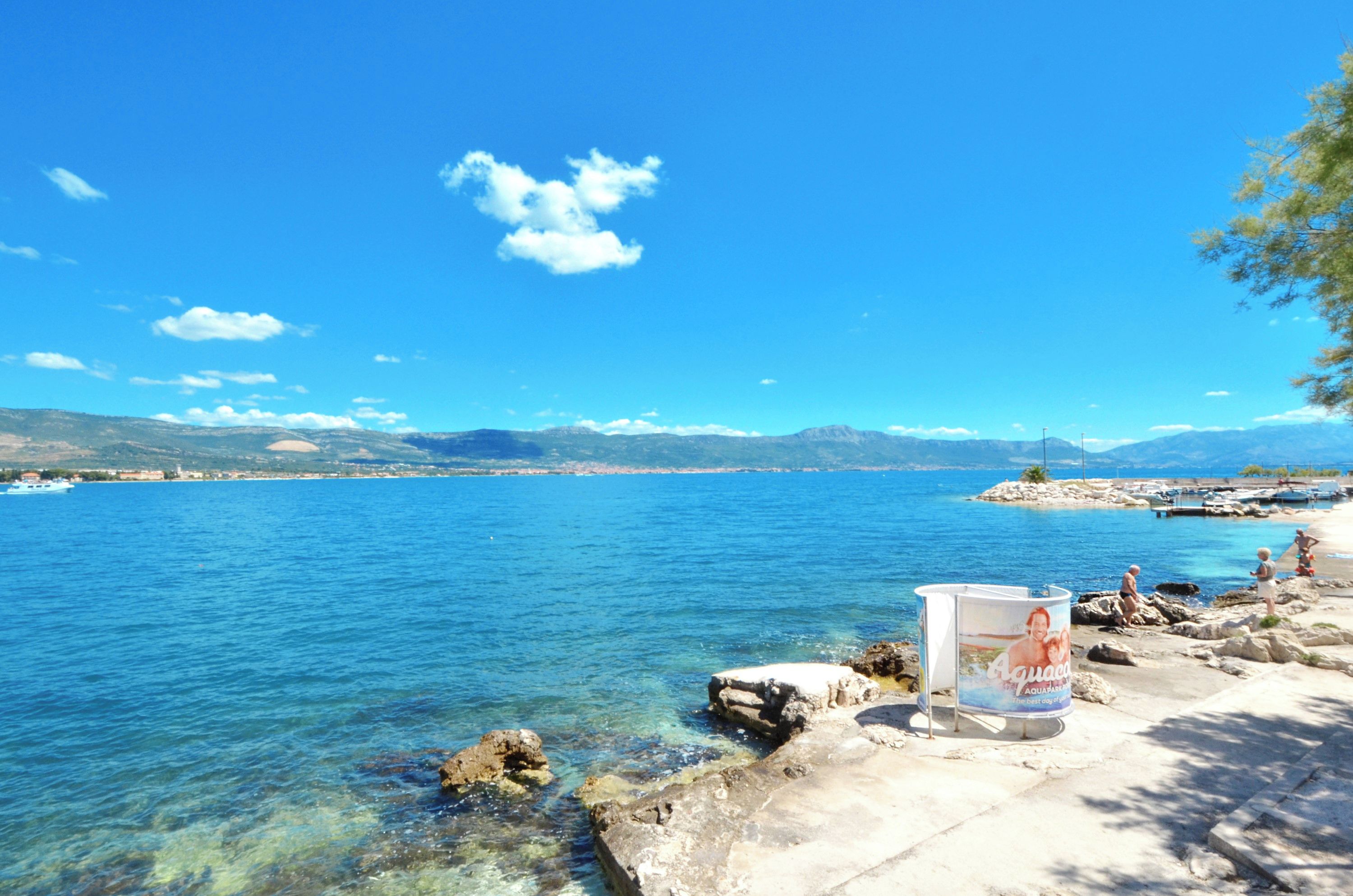 Vista costera con aguas azul cristalino, costa rocosa y montañas al lejano.