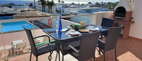 A terrace with a table set for dining, overlooking a swimming pool and a view of the sea.