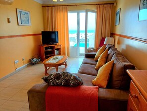 A living room with a sofa, a television, a table, and a view of the sea through a glass door. - Villa Zen with sea view (Puerto del Carmen)