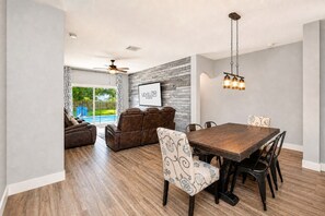 A spacious living area with a dining table, comfortable seating, a ceiling fan, and a view of a swimming pool. - Heated Pool~Windsor Resort~Near Disney~Game Room (Kissimmee)