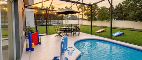 A swimming pool with a basketball hoop, outdoor seating, and string lights.