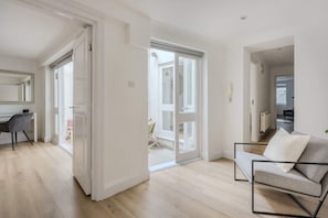 A modern living room with a sofa, a desk, and a chair. There are sliding glass doors leading to an outdoor area. - 2-Bed Flat near Regent's Park - Patio - Sleeps 6 (London)