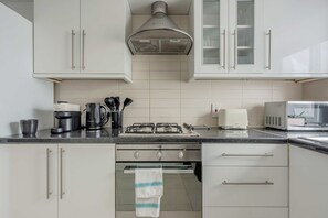 A modern kitchen with white cabinets, a gas stove, a coffee maker, and a microwave. - 2-Bed Flat near Regent's Park - Patio - Sleeps 6 (London)