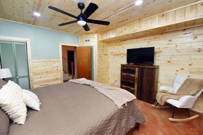 Ein Schlafzimmer mit einem Bett, einem Fernseher auf einer Holzkommode, einem Schaukelstuhl und einem Deckenventilator.