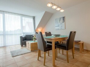 Ein modernes Wohnzimmer mit Essbereich, ausgestattet mit einer Couch, einem Esstisch mit Stühlen, einer Lampe und einem Gemälde an der Wand.