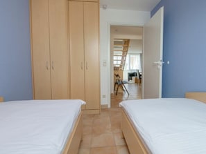 Ein Schlafzimmer mit zwei Betten, Holzschränken und einer Treppe, die in einen oberen Bereich führt.