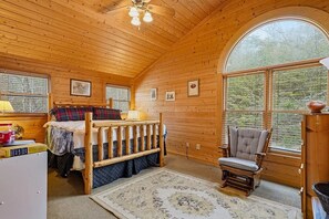Une chambre confortable dans un chalet, avec un plafond en bois, un lit doté d’une tête de lit, une chaise et une grande fenêtre donnant sur le paysage extérieur.