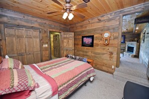 A wooden-paneled room with a bed, a ceiling fan, a clock, and a fireplace. - Work Hard Play Hard- View-Gameroom (Blue Ridge)