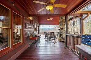 A wooden deck with a table and chairs, a ceiling fan, and a stone wall. - Work Hard Play Hard- View-Gameroom (Blue Ridge)