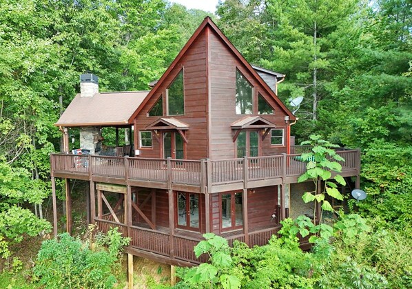 Une cabane en bois à deux étages, dotée d’un balcon à l’étage supérieur, et entourée d’une forêt dense.