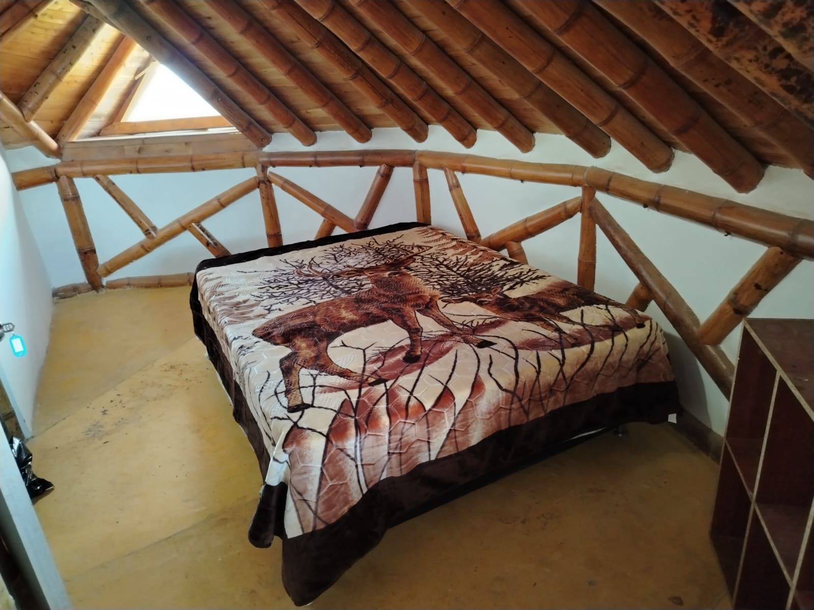 Una habitación con techo inclinado, una cama con colcha estampada y estructura de techo de madera.