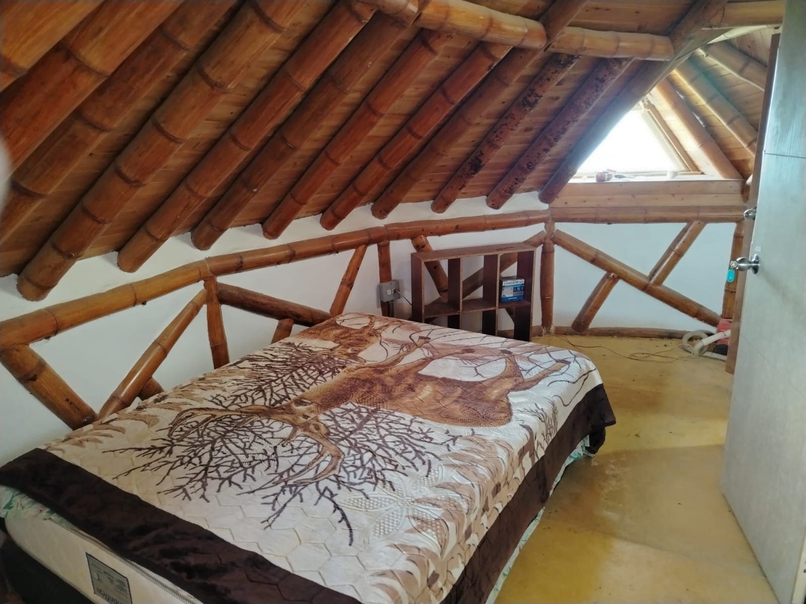 A room with a sloped wooden ceiling, a bed with a patterned bedspread, and a small wooden shelf.
