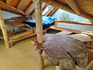 A wooden interior with a sloped ceiling, a bed with a blue cover, and a large wooden table.