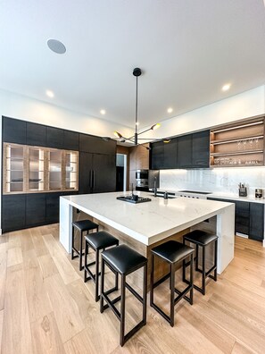 Una cocina moderna con una isla grande, taburetes de bar, armarios oscuros y una encimera de madera.