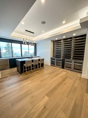 A modern kitchen with a central island, bar stools, large windows, and a view of the outdoors.