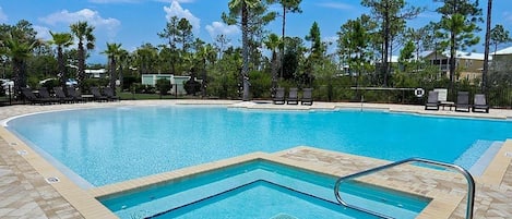 A swimming pool with a tiled deck, surrounded by palm trees and lounge chairs.