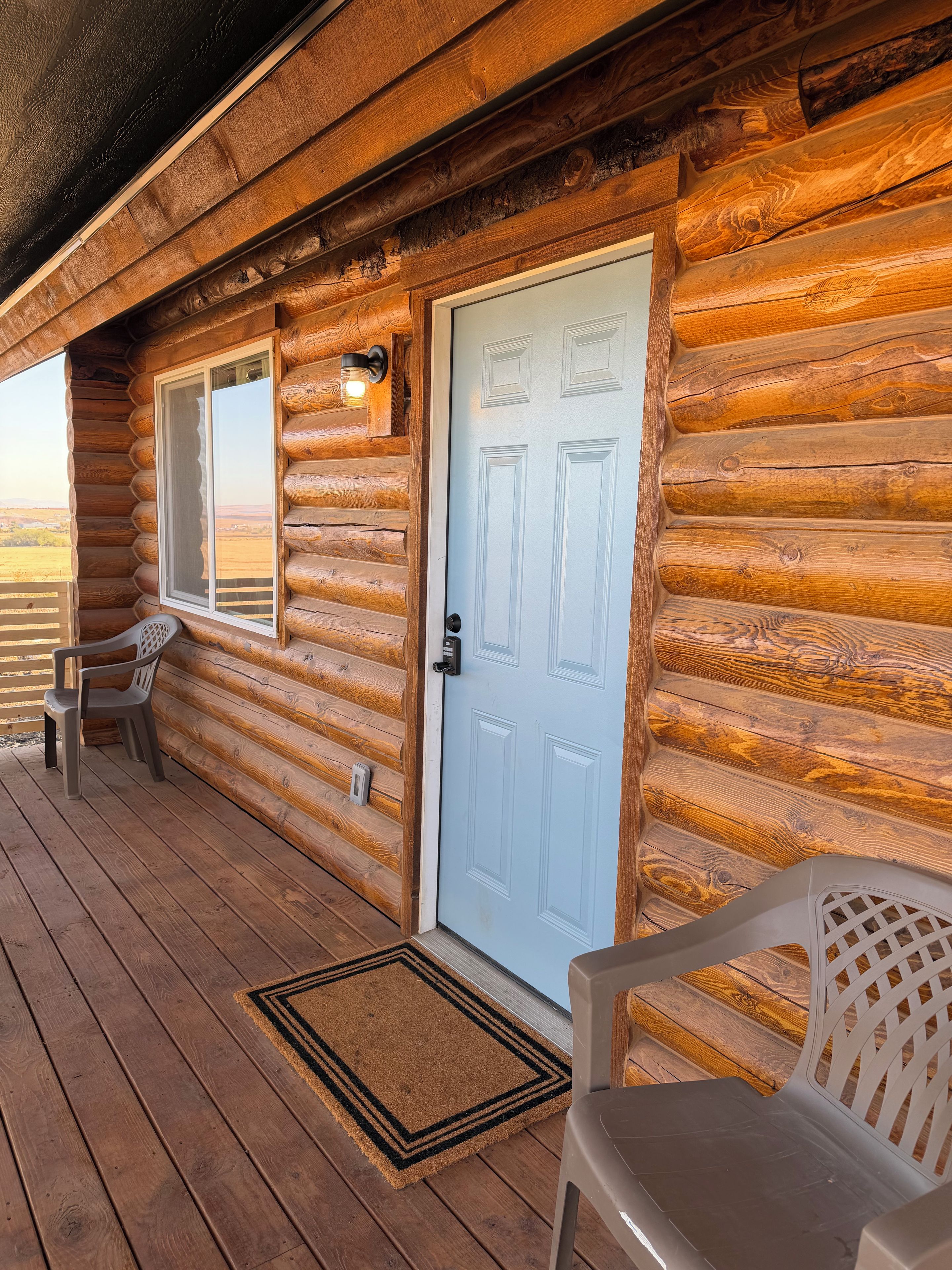 A log cabin with a wooden porch, a blue door, and two chairs.