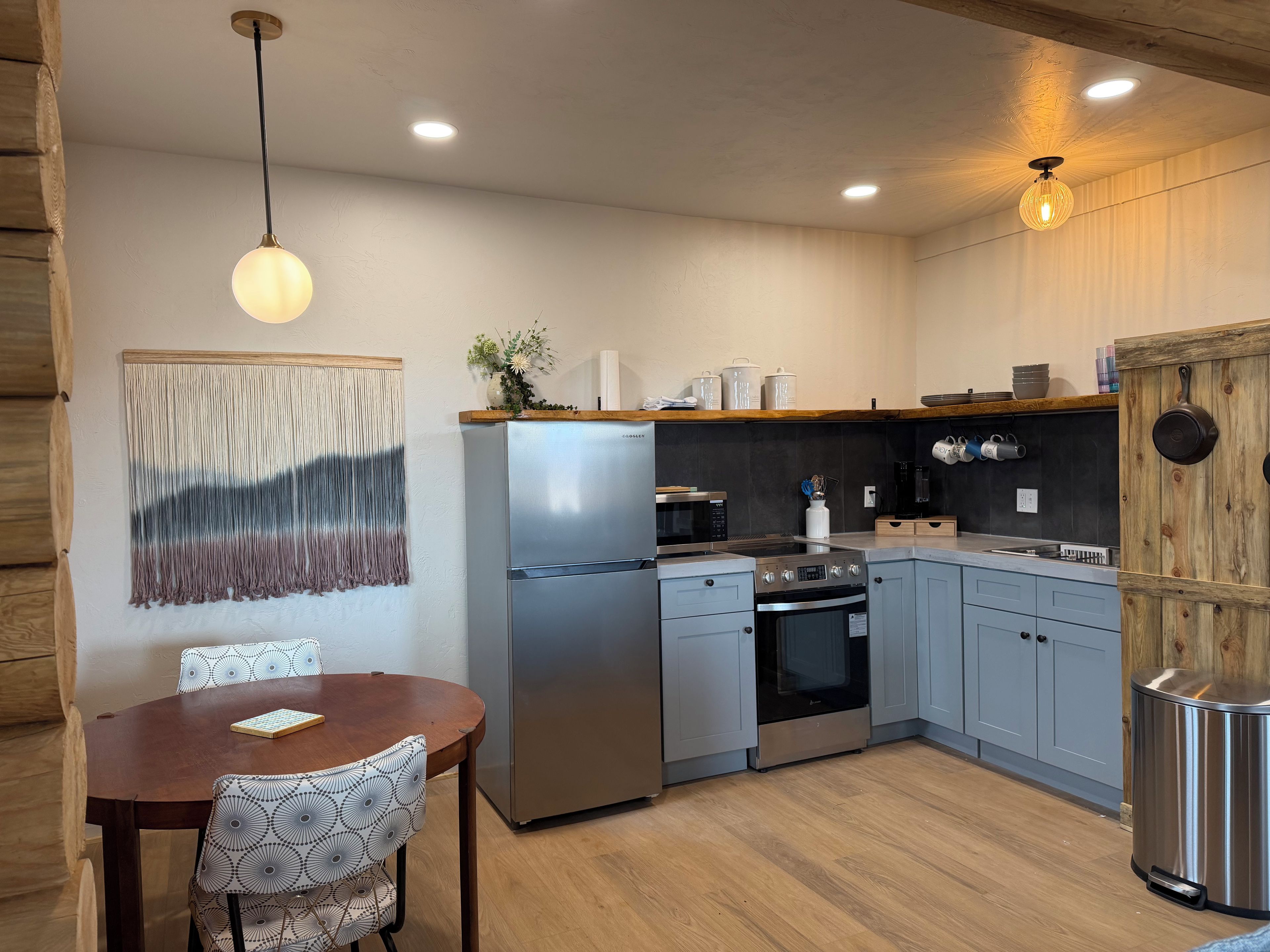 A modern kitchen with a stainless steel refrigerator, oven, and microwave, wooden cabinets, and a dining table with chairs.