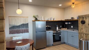 A modern kitchen with a stainless steel refrigerator, oven, and microwave, wooden cabinets, and a dining table with chairs.