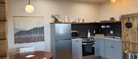 A modern kitchen with a stainless steel refrigerator, oven, and microwave, wooden cabinets, and a dining table with chairs.
