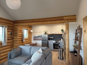 A log cabin interior with a living area, kitchen, and wooden walls.