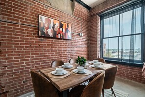A dining area with a brick wall, a large window, and a painting. - Spacious Loft downtown STL with  free parking, fitness centre & rooftop terrace. (St. Louis)