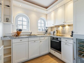 A modern kitchen with white cabinetry, a granite countertop, and a built-in oven. - Holiday Apartment Watt'n Blick (Sylt)
