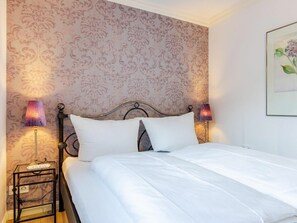 A neatly made bed with white linens, a metal headboard, and two bedside lamps. - Holiday Apartment Watt'n Blick (Sylt)