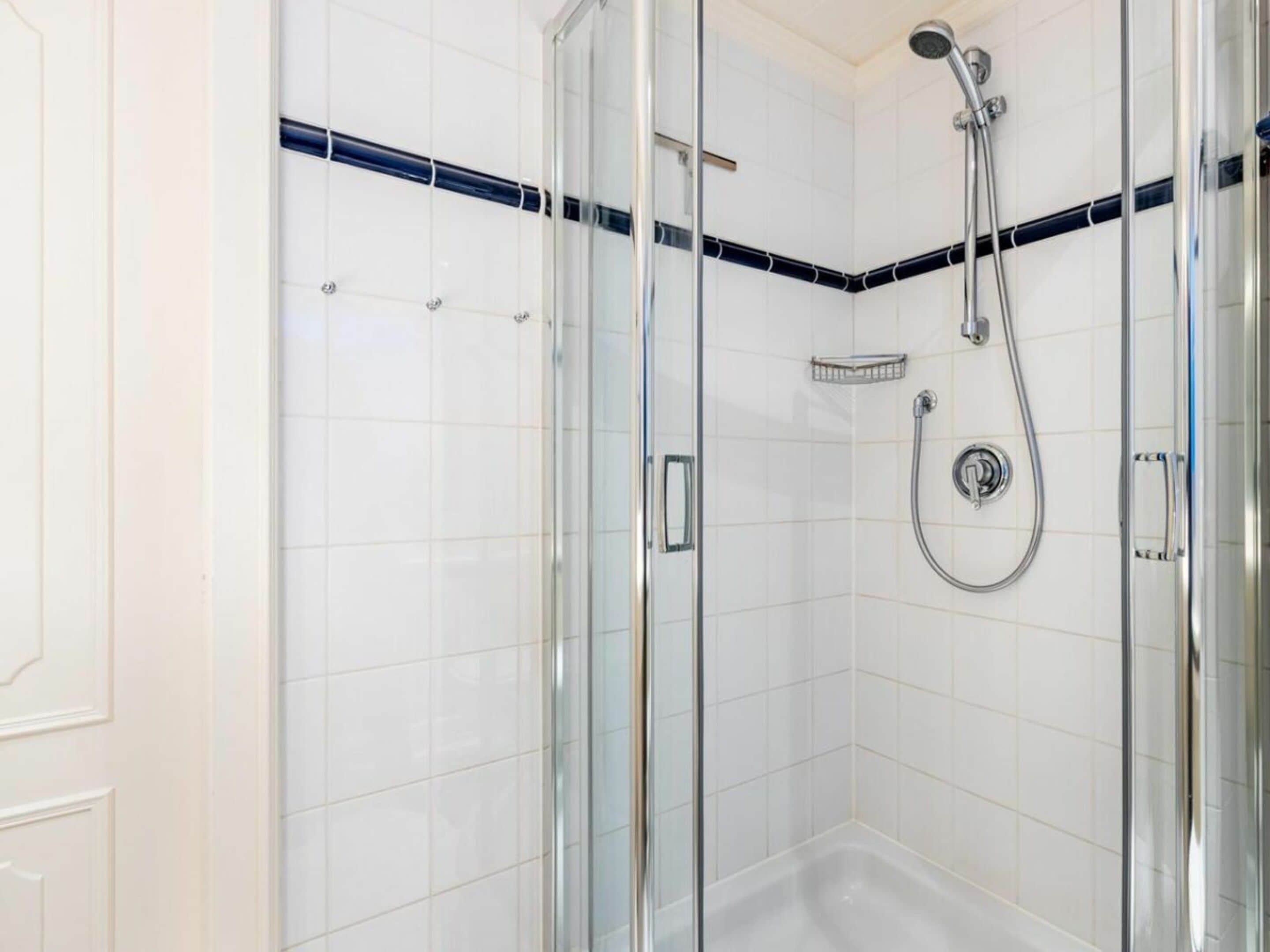 A glass-enclosed shower area with a handheld showerhead and a wall-mounted faucet.
