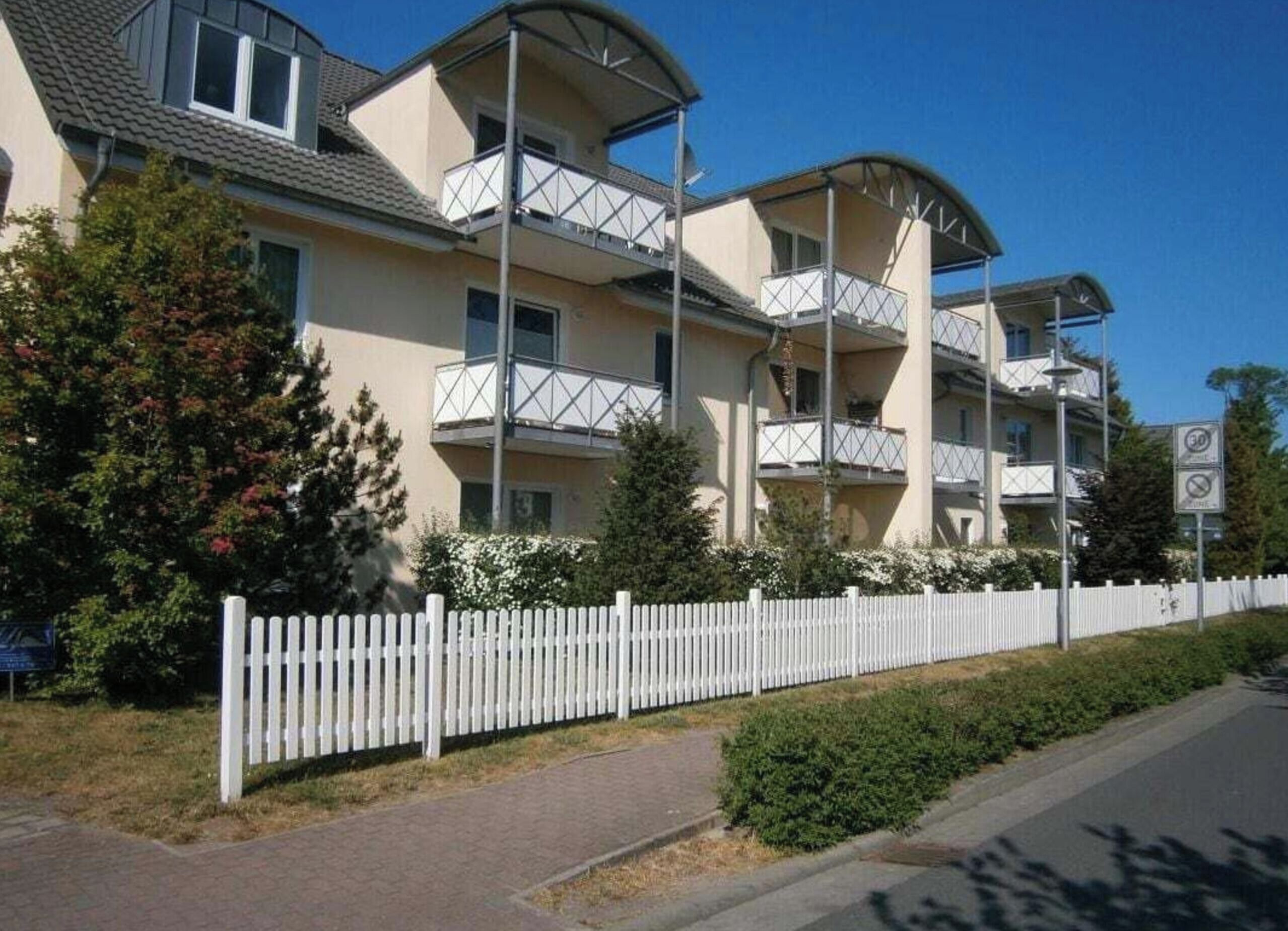 A multi-story residential building with balconies, a white picket fence, and a clear sky.