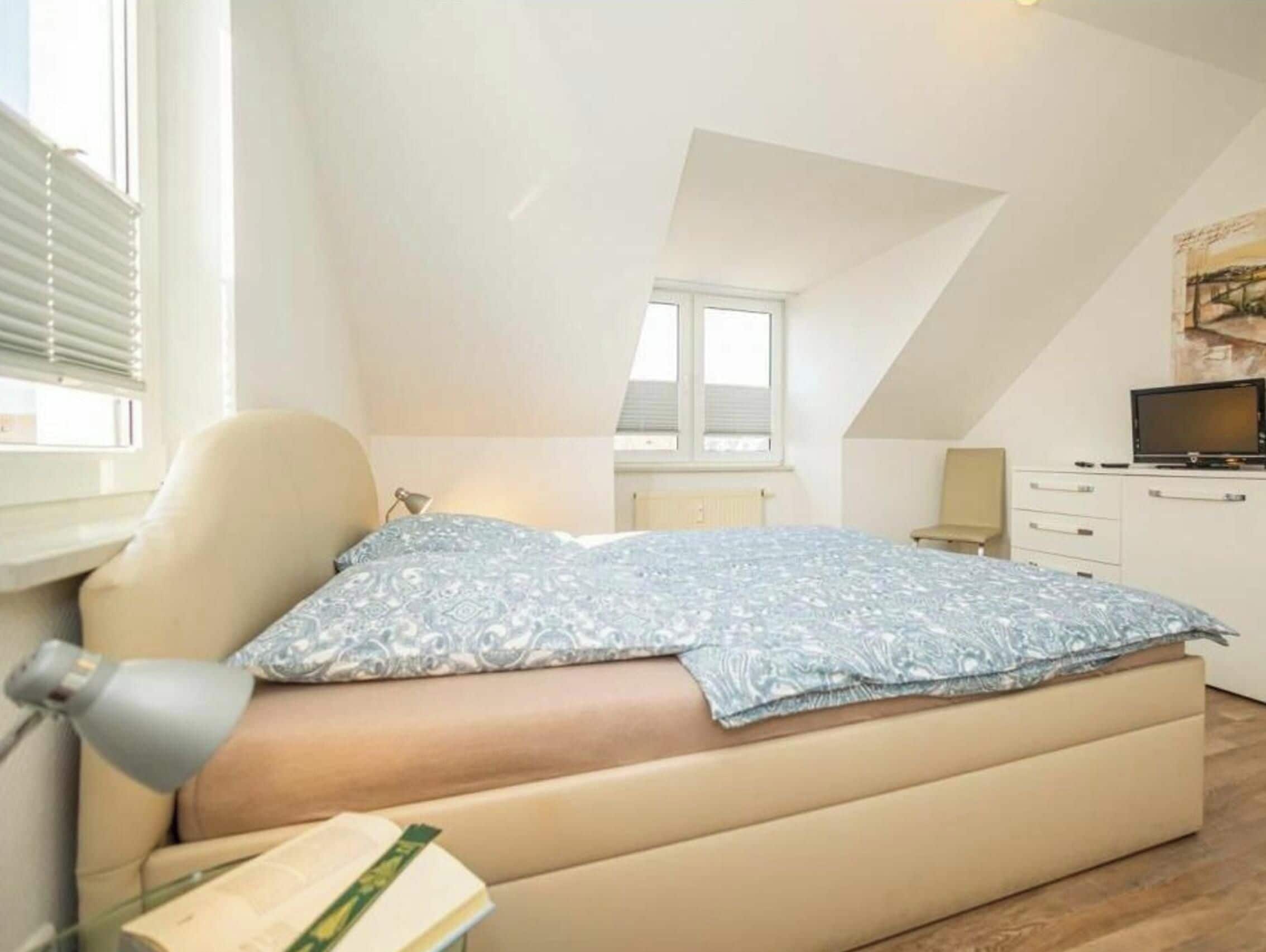 Un dormitorio con cama, escritorio, silla, ventana y televisor.