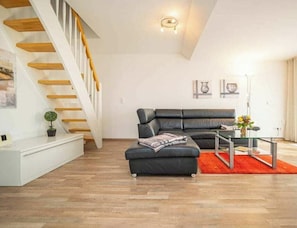 A modern living room with a black leather sofa, a glass coffee table, and a staircase with wooden steps. - Apartment 16 on the 2nd Floor of Haus Stranddistel (Zingst)