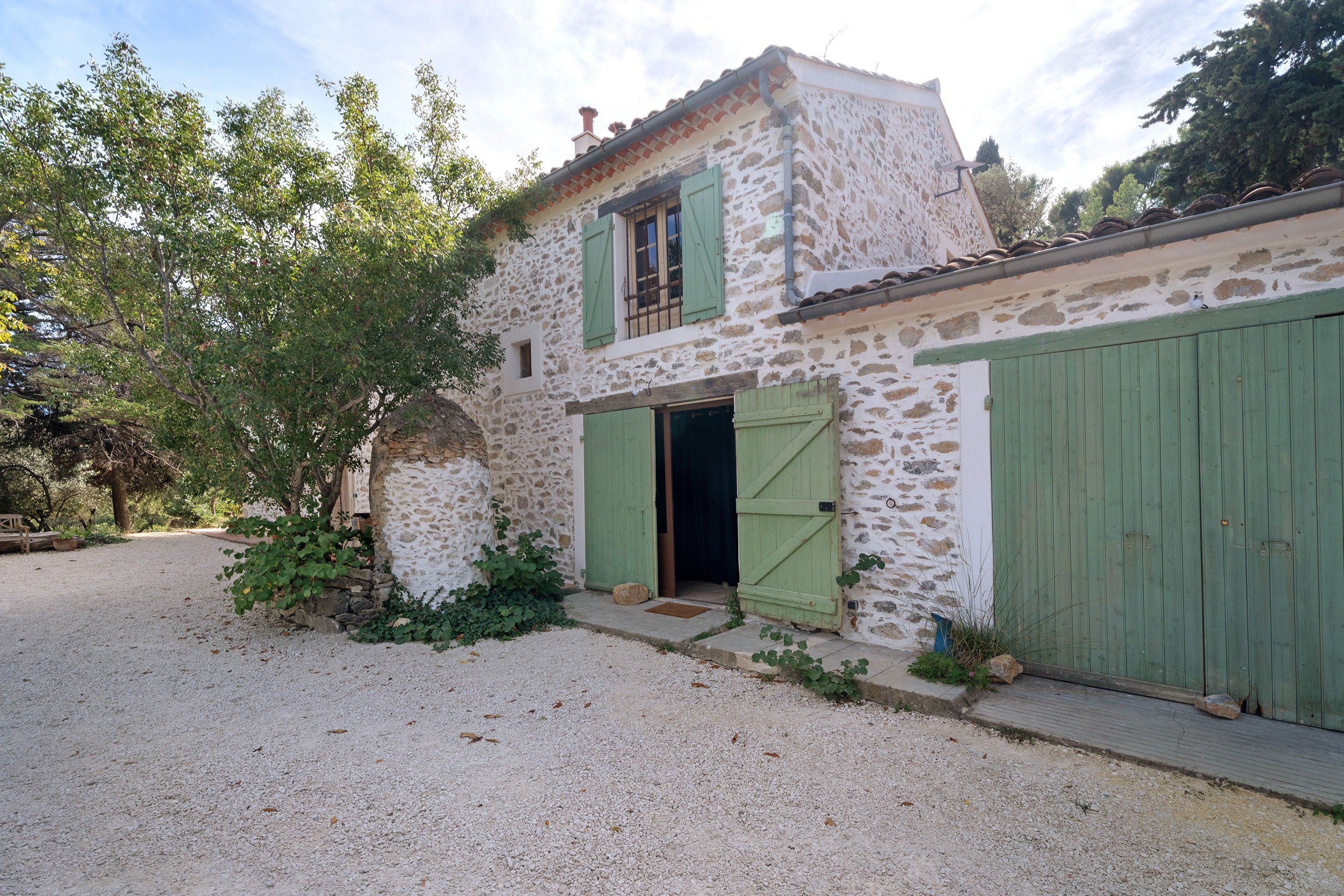 Un edificio de piedra con camino de grava y contraventanas verdes.
