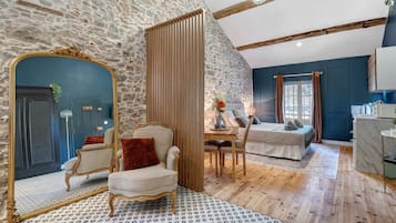 Una habitación con pared de piedra, un espejo con marco dorado, una silla de madera, una cama y una mesa de comedor con sillas.