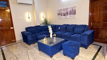 A living room with a sectional sofa, a glass coffee table, and a marble floor.