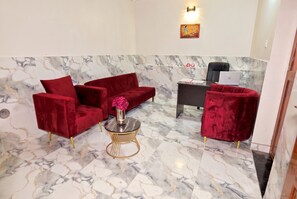 A lobby with marble flooring, red velvet sofas, a small round table with a vase of flowers, and a desk with a laptop.