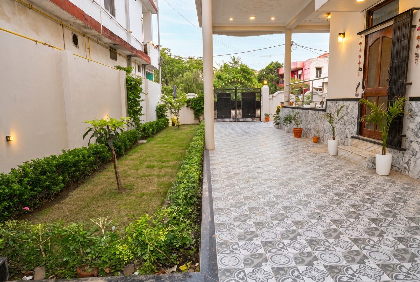 A covered outdoor area with a patterned floor, potted plants, and a gated entrance.