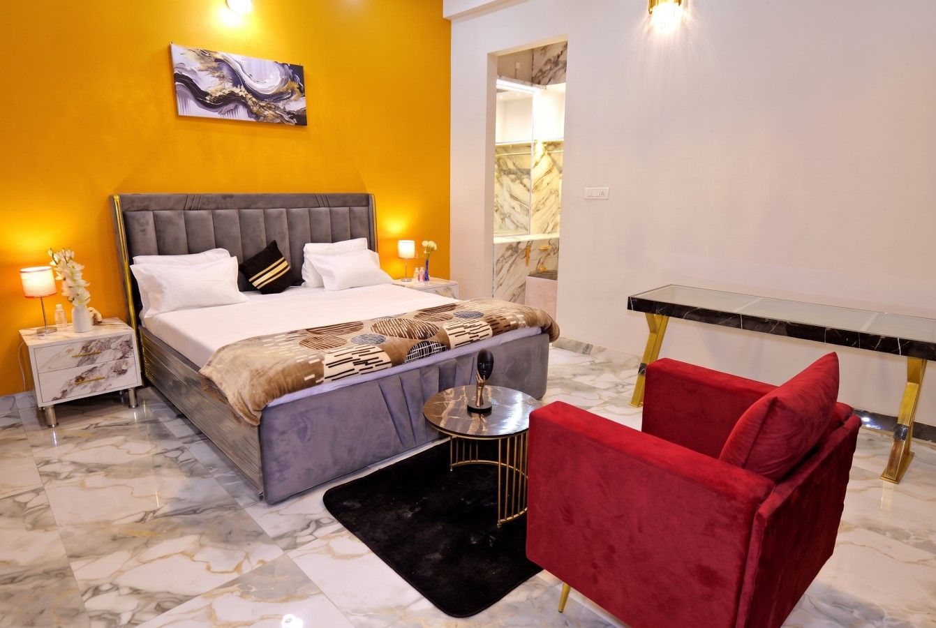 A hotel room with a bed, a red chair, a small round table, and a marble floor.