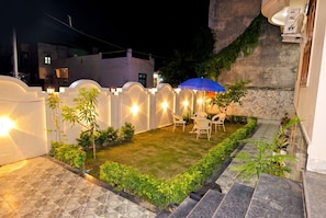 A well-lit outdoor patio area with a small lawn, seating, and a blue umbrella.