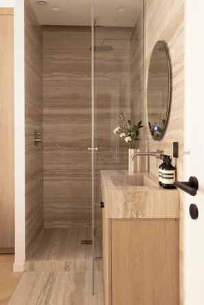Ein modernes Badezimmer mit einer gläsernen Dusche, einem hölzernen Waschtisch mit Spiegel und einer kleinen Vase mit Blumen.