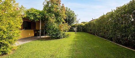 Un área verde y bien cuidada, con setos en un lado y un edificio con fachada amarilla en el otro.