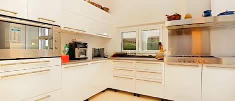 A modern kitchen with white cabinetry, a built-in oven, and a window with a view of greenery.