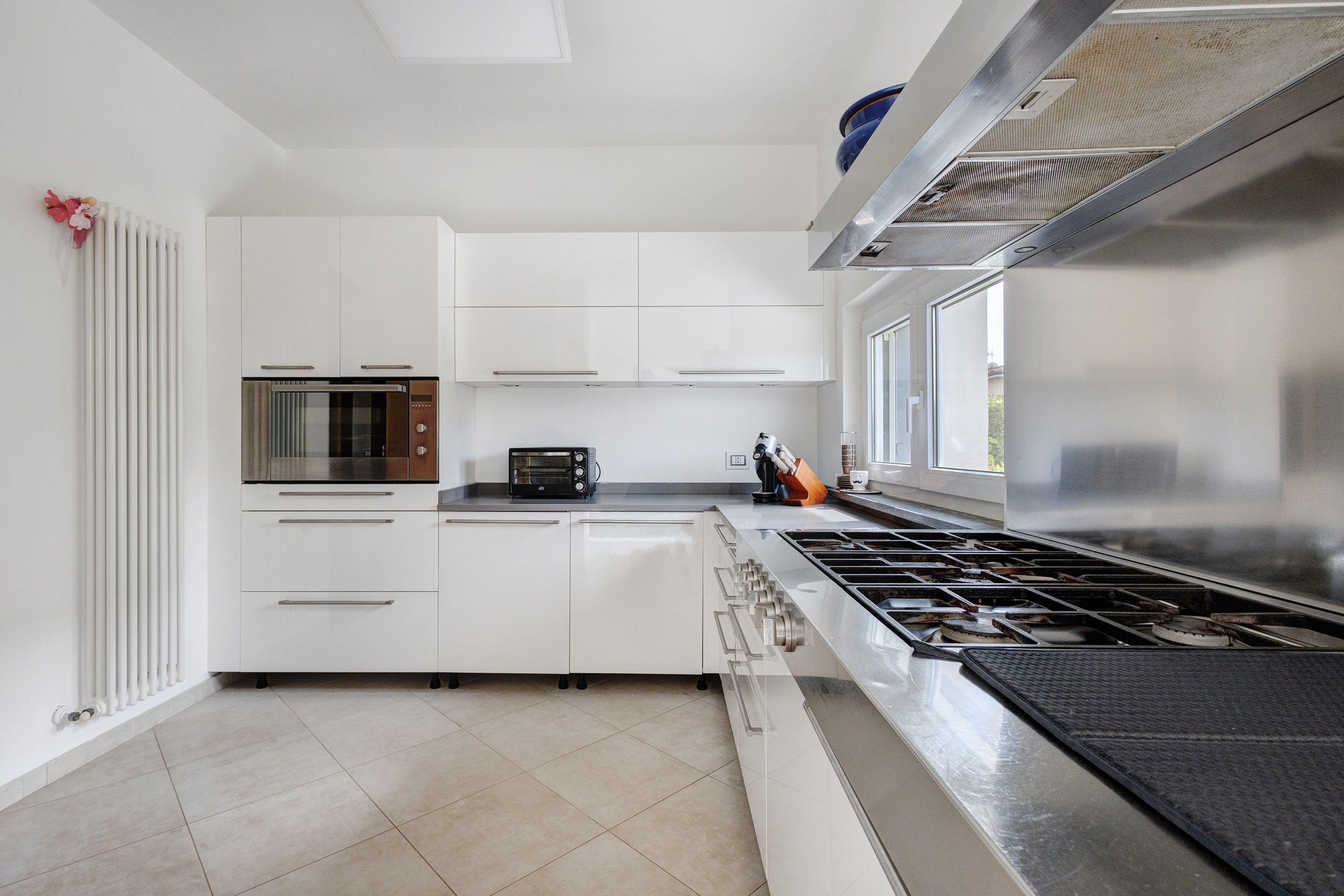 A modern kitchen with white cabinetry, a built-in oven, a stovetop, and a window providing natural light.