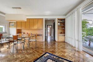 Een moderne keuken met houten kastjes, een eethoek met een glazen tafel en een uitzicht door een groot raam.