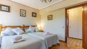 Ein Hotelzimmer mit zwei Betten, einem hölzernen Kopfteil, einer Chandelüster und gerahmten Kunstwerken an den Wänden.