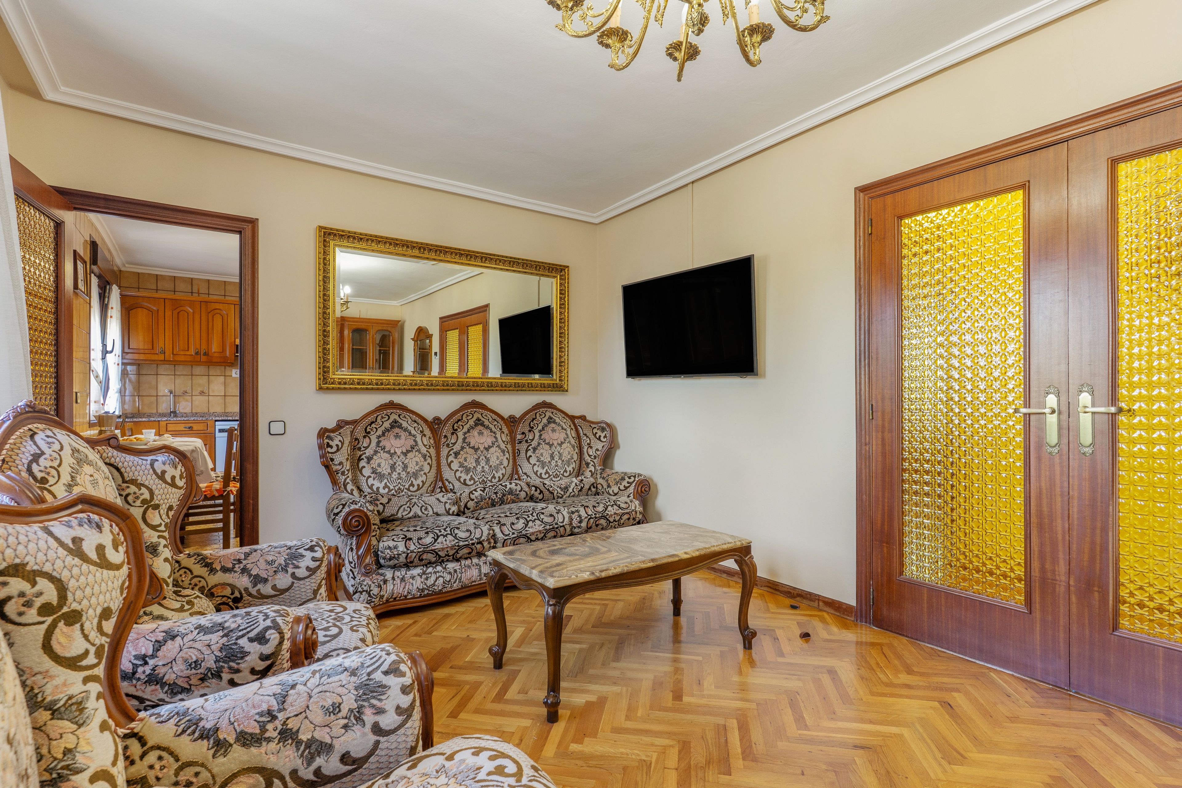 A room with a sofa, chairs, a television, a mirror, and a door with a golden pattern.