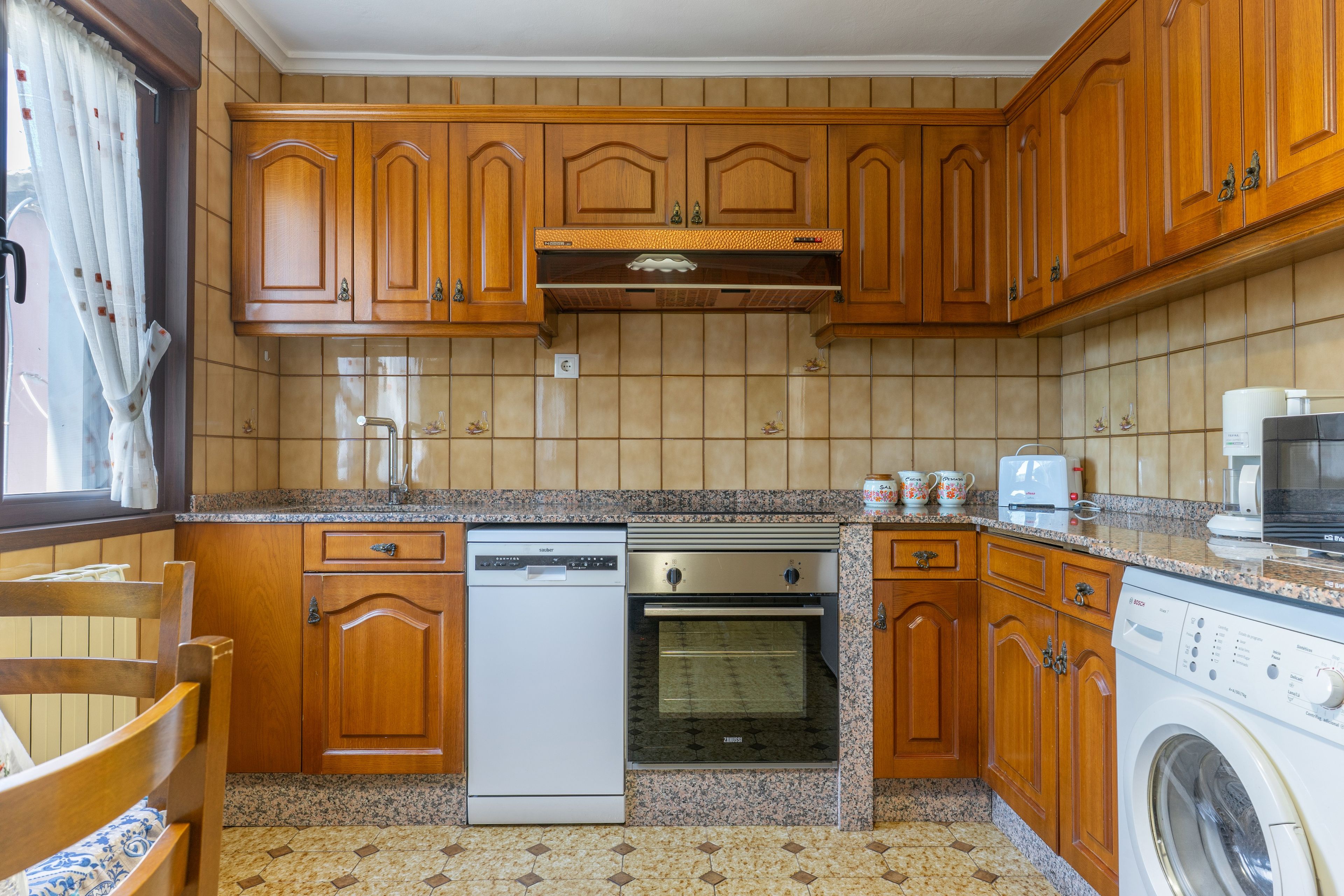 Una cocina con armarios de madera, lavavajillas, horno, lavadora y cafetera.