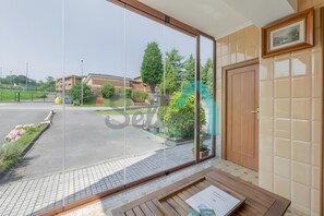A room with a large sliding glass door leading to a parking area, a wooden bench, and a door with a small window.